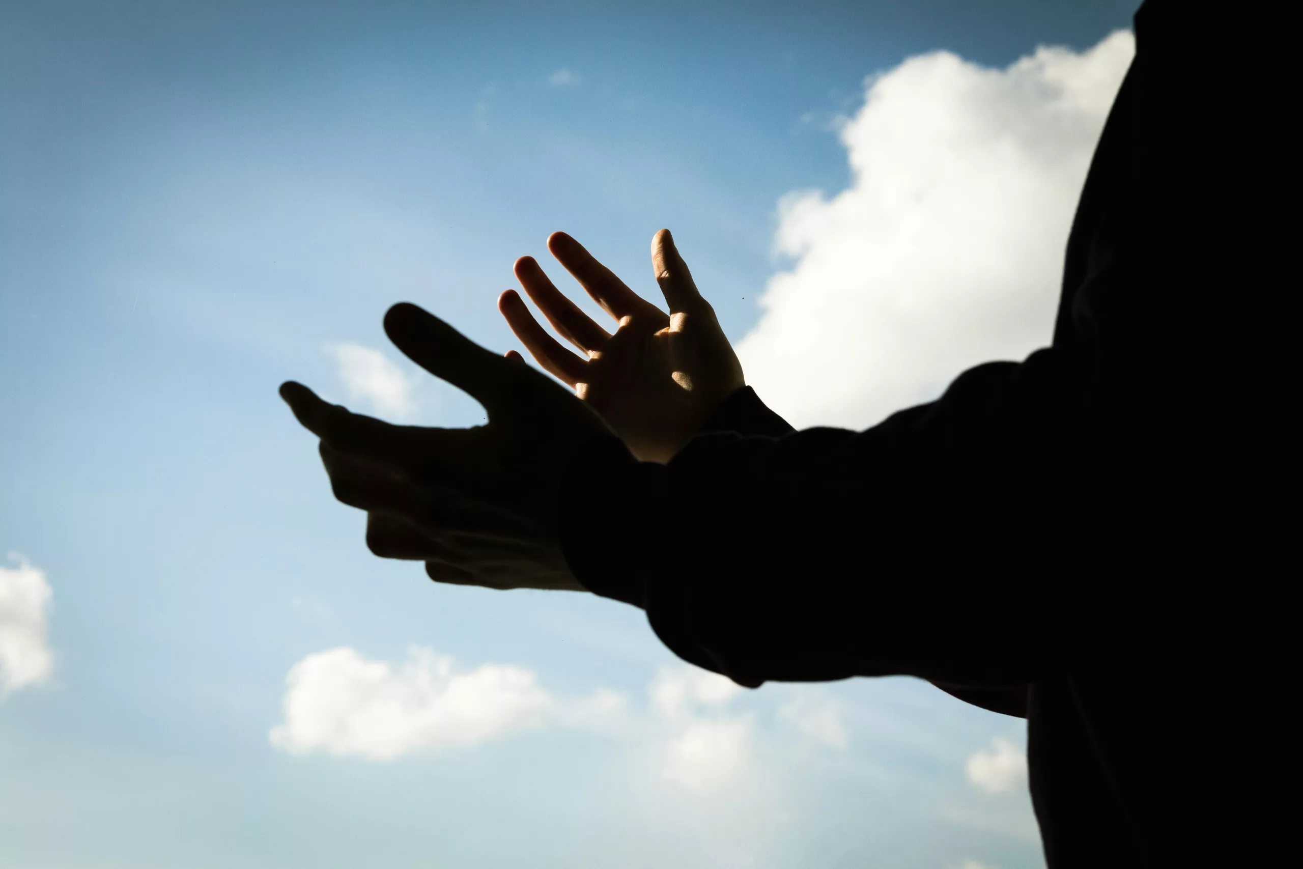 Open hands reaching toward a bright sky