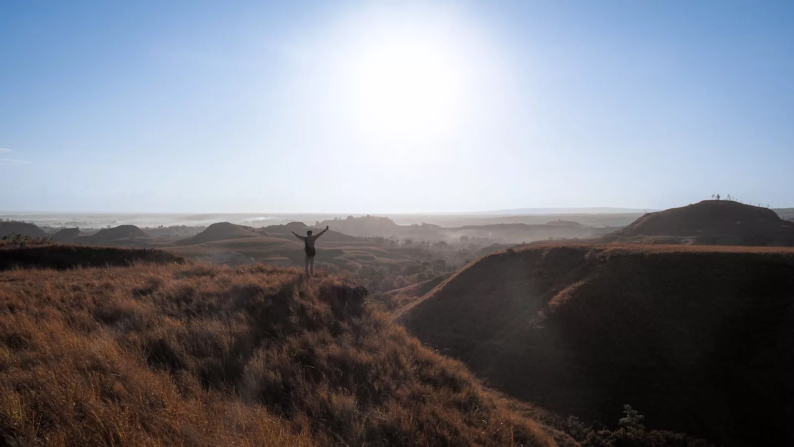 A person with arms raised on a hilltop at sunrise