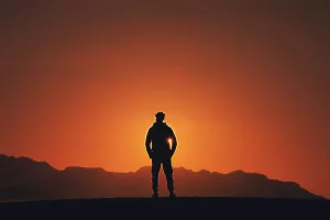 Silhouette photography of person standing on platform with mountain background during golden hour