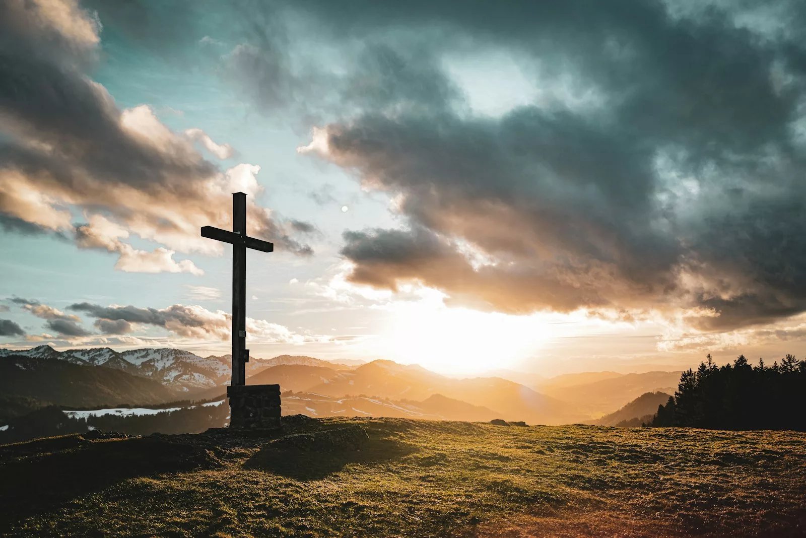 A cross on a hill against a dramatic sunset sky