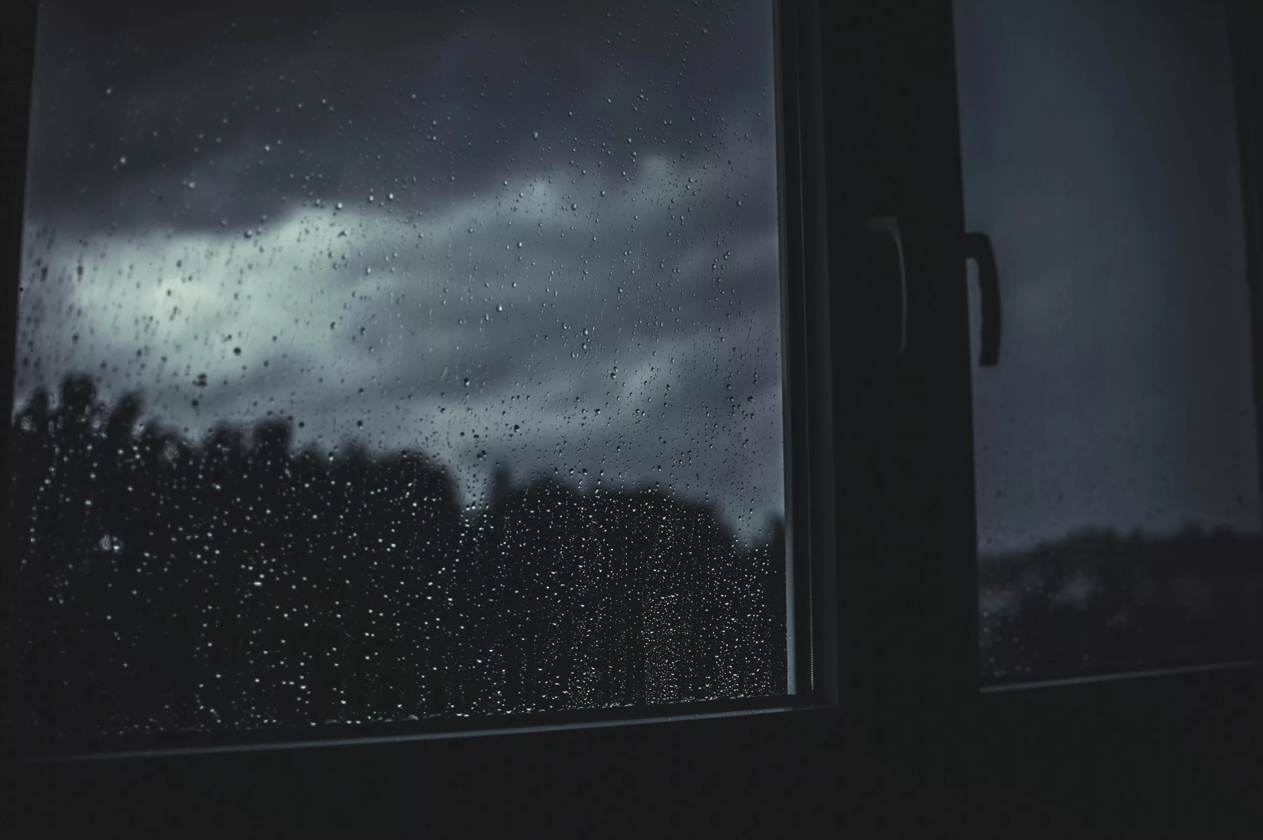 Rain drops on a dark window with a stormy sky beyond