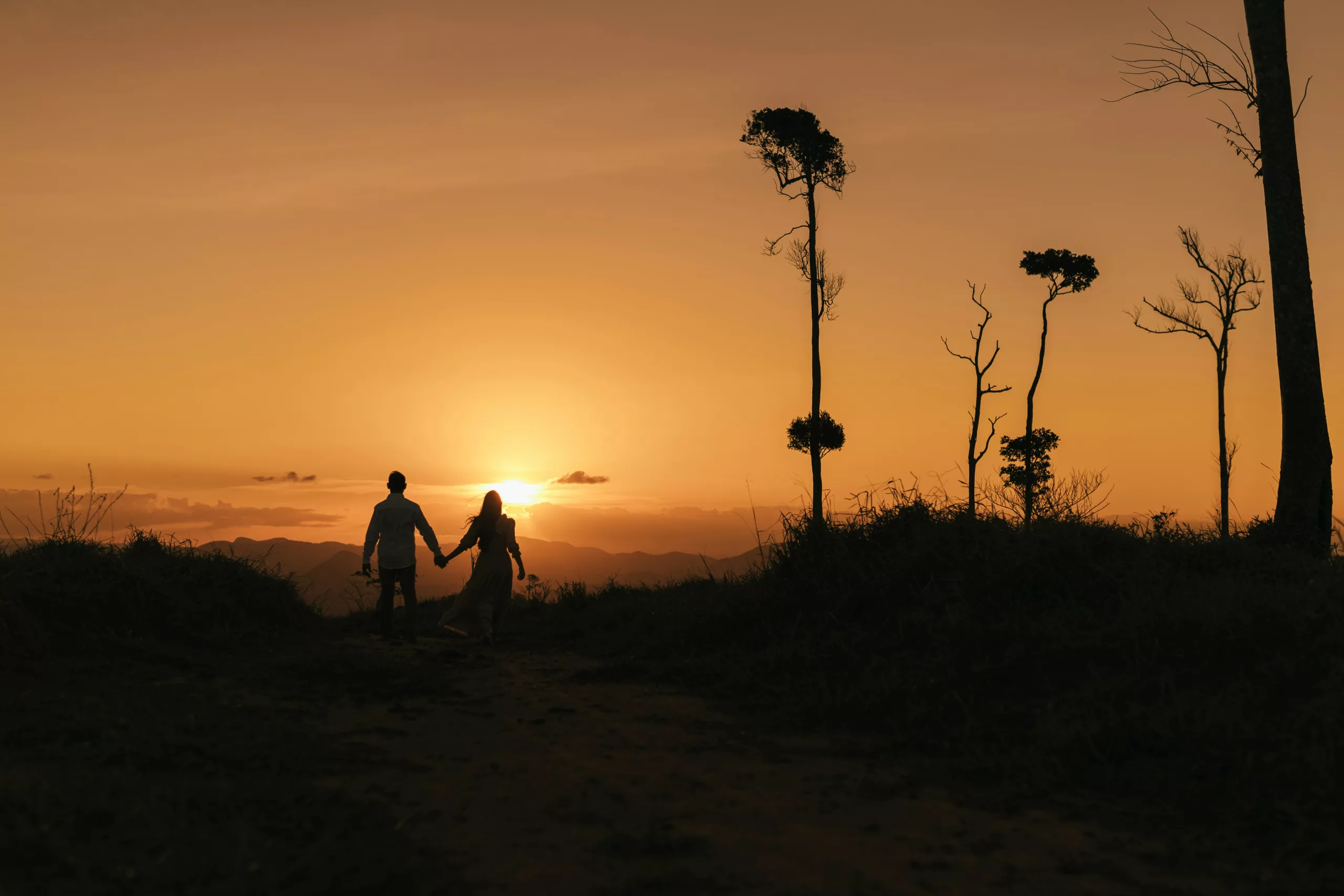 A couple holding hands walking toward a sunset