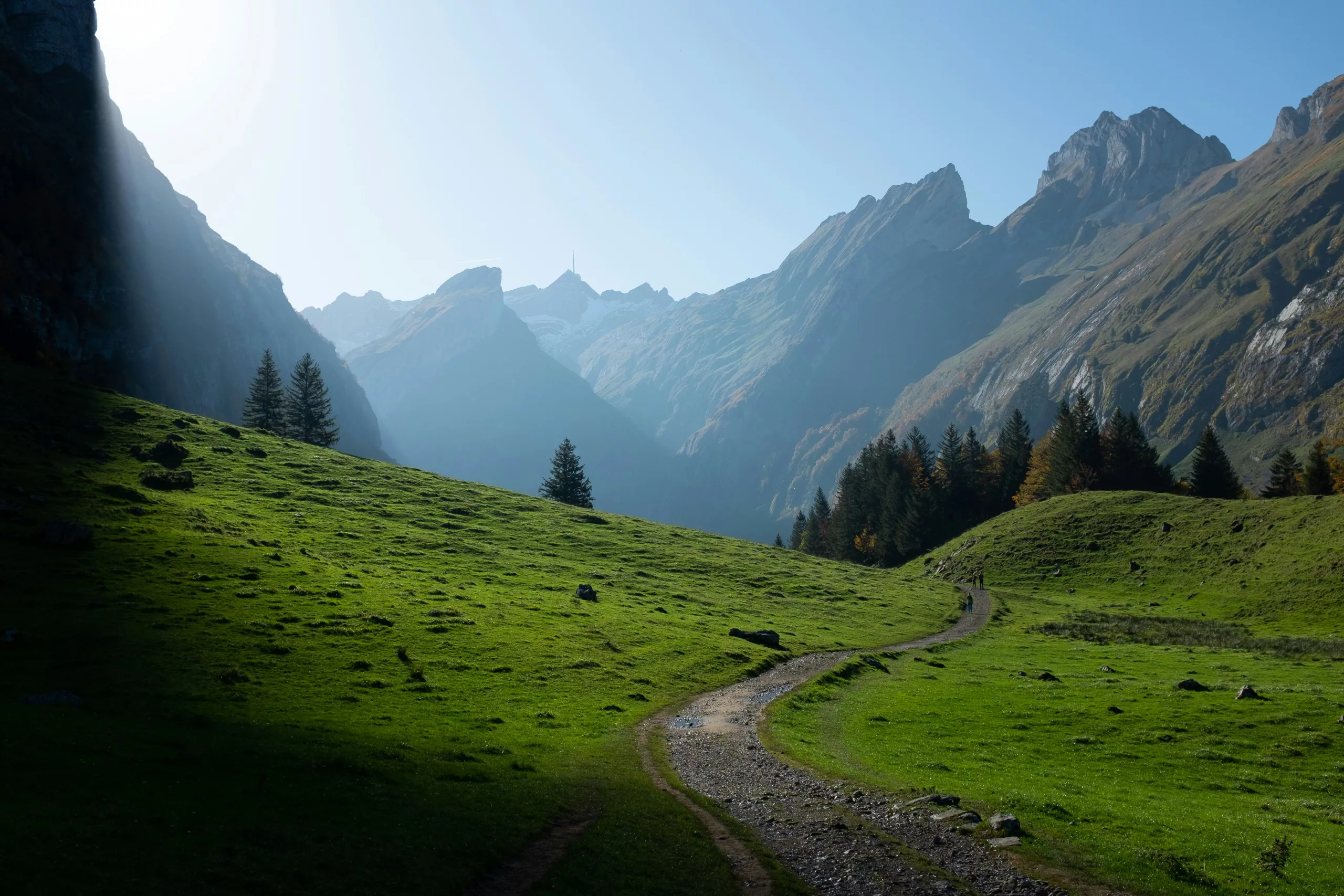 A path winding through a green alpine valley toward mountains